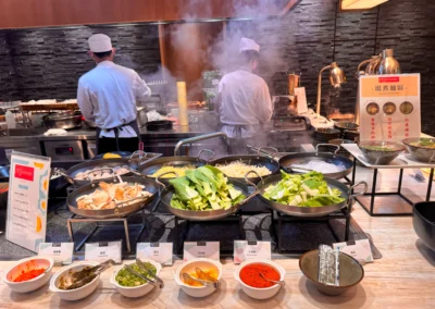 Sizzling steam rising at the live noodle bar with fresh bok choy, mushrooms, and noodles made hot and fresh while you watch.