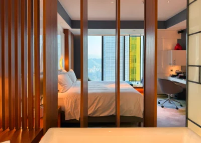 View from the bathroom into the bedroom in the Fabulous Room, Corner Unit at W Taipei, featuring a king bed, city skyline, and modern wood panel dividers.