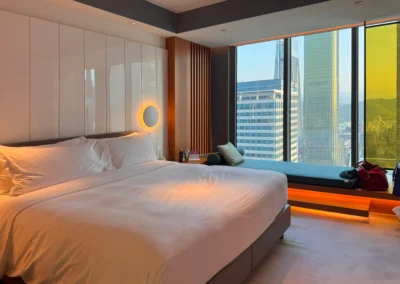 Bedroom in the Fabulous Room, Corner Unit at W Taipei, featuring a king bed, panoramic city views, and a built-in window daybed with ambient lighting.