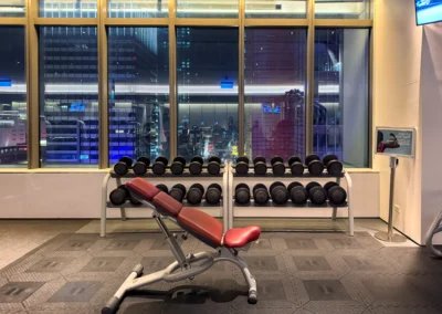 Free weights and bench press area in the FIT gym at W Taipei, with a nighttime cityscape view.